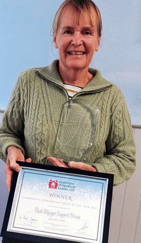 Mrs Mary Whibley, of the Bude Refugee Support Group, with a trophy and certificate marking its crowning as Community Sponsorship Group of the Year 2019